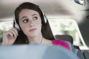 Seorang traveler mendengarkan musik dengan headphone sambil menikmati pemandangan alam dari jendela mobil.