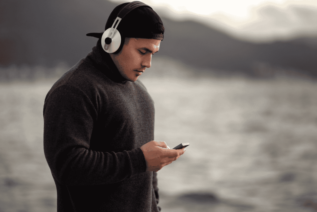 Seorang traveler mendengarkan musik dengan headphone sambil menikmati pemandangan pantai.