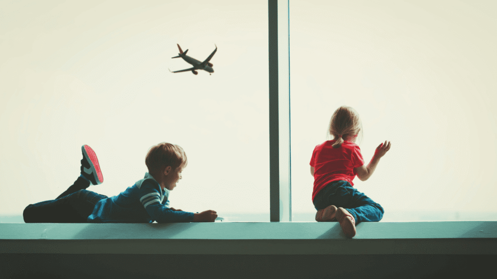 Anak kecil melihat pesawat dari jendela bandara, mempersiapkan liburan pertamanya ke luar negeri